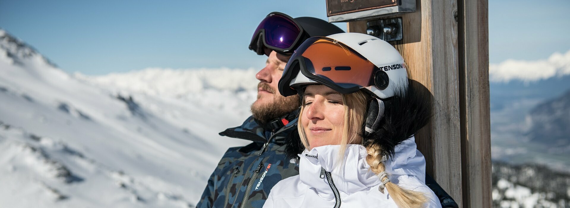 Pärchen sitz mit Skihelm in der Sonne und haben Augen geschlossen