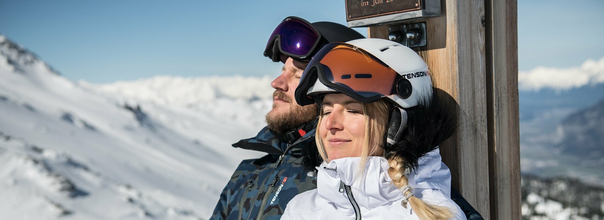 Pärchen sitz mit Skihelm in der Sonne und haben Augen geschlossen