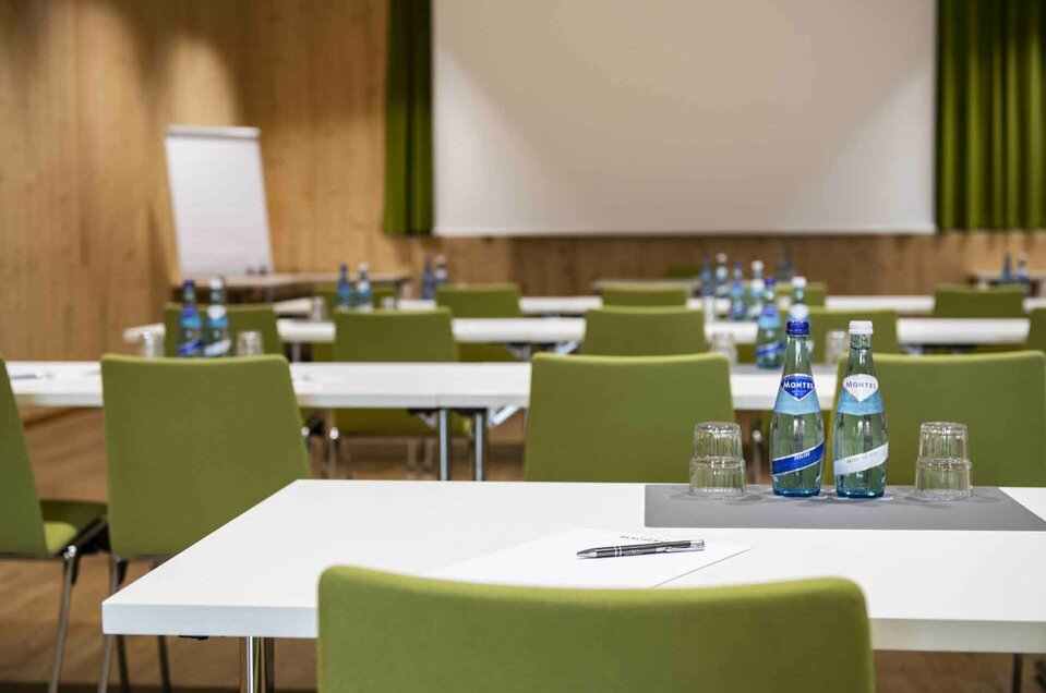 Seminarraum mit Leinwand, Flipchart, Tischen, Schreibbedarf und Wasser